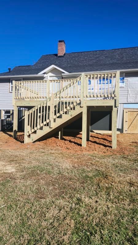 Newly built wooden deck with stairs against a house, brown yard, clear blue sky.