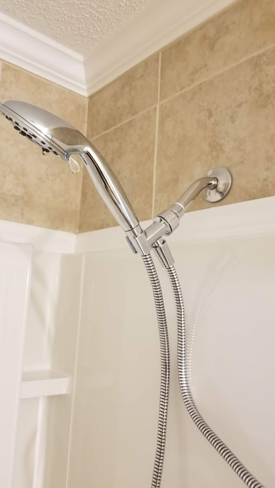 Chrome shower head and hose in a white and tan tiled shower.