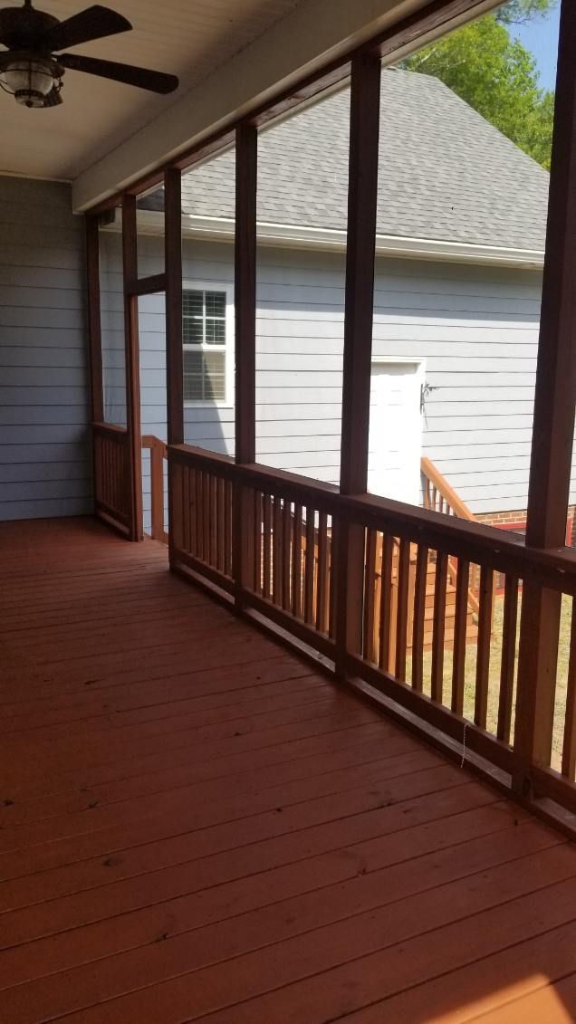 Screened porch with reddish-brown wood railings and deck, gray siding, and a view of a gray building.