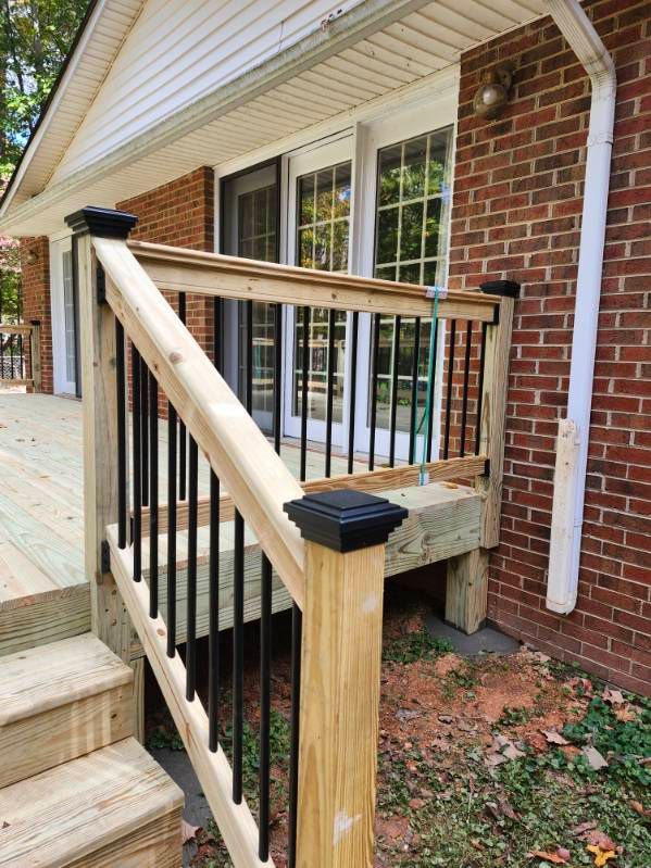 Wooden deck with black railing and steps against a brick house.