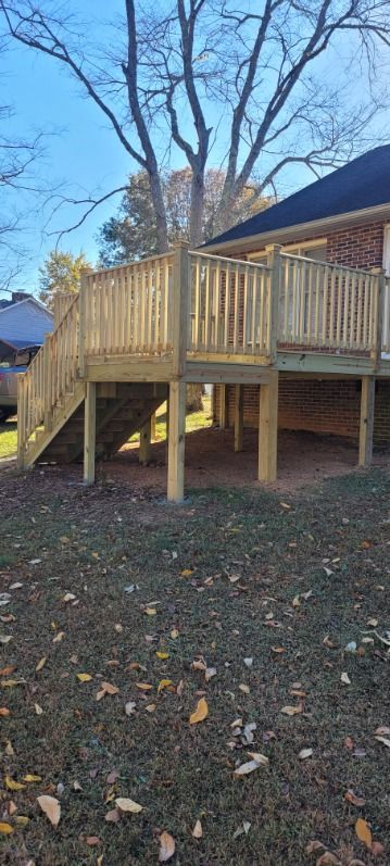 Newly built wooden deck with stairs in a yard with sparse grass and a large tree.