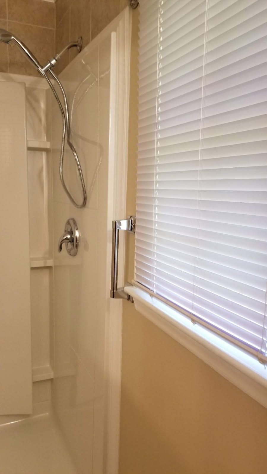 Shower stall with chrome fixtures and window with white blinds.