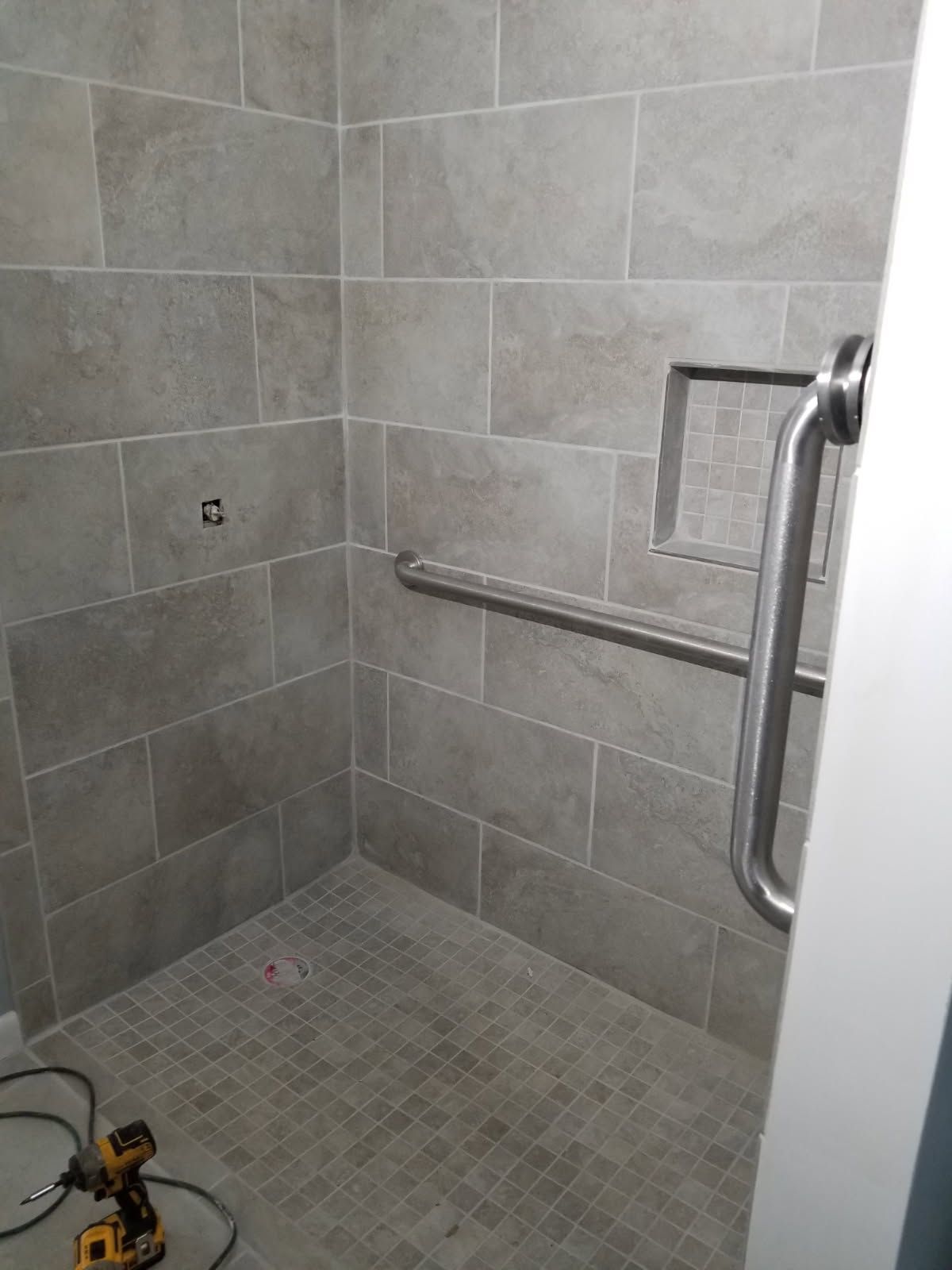 Tile shower stall with grab bar and recessed shelf.