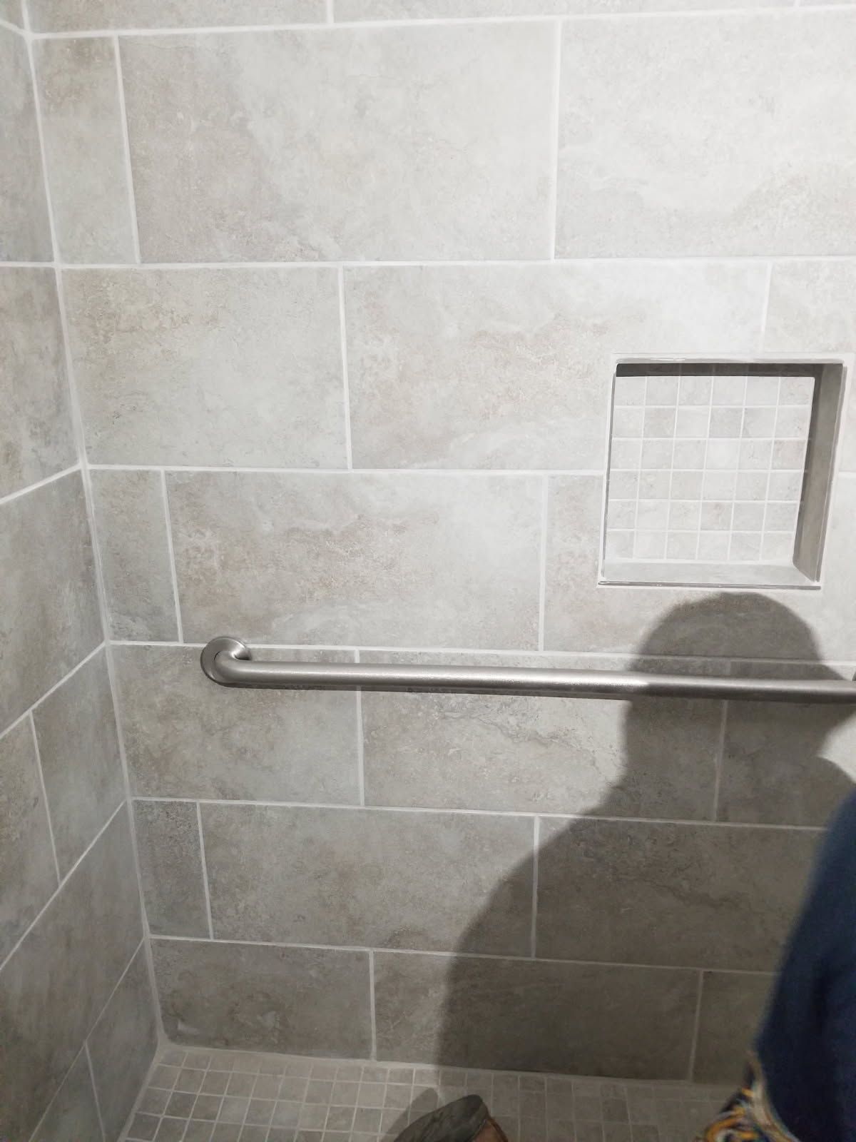 Shower with gray rectangular tiles, a recessed shelf with small tiles, and a horizontal grab bar.
