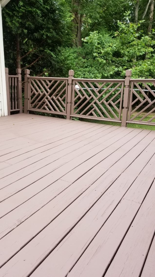 Brown wooden deck with decorative railing, overlooking green trees.