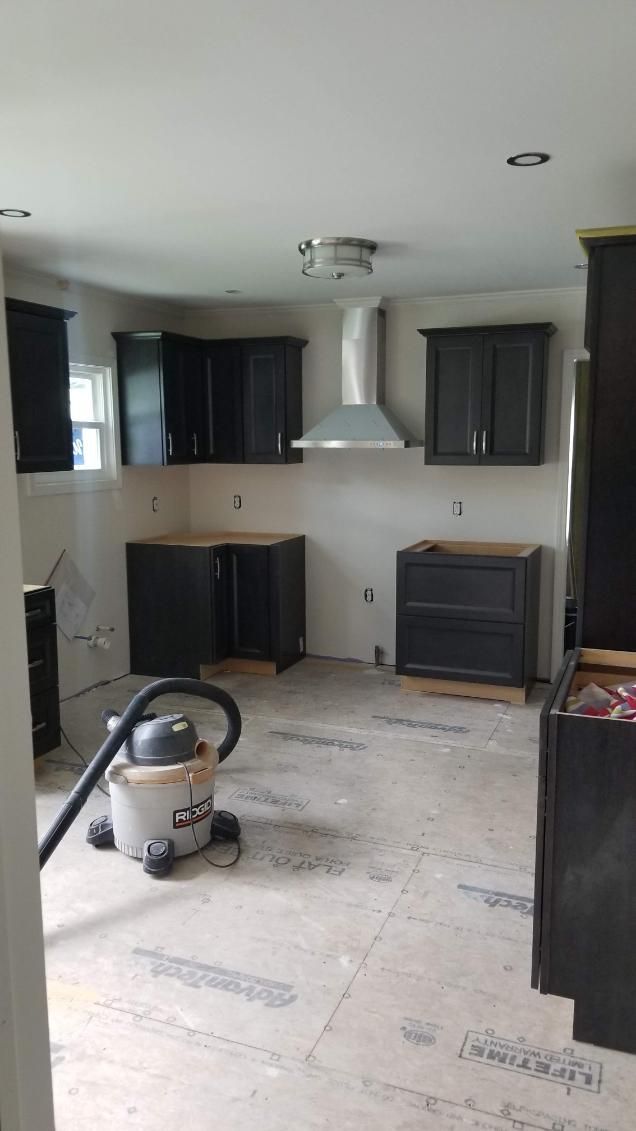 Kitchen remodel in progress: dark cabinets, stainless steel range hood, vacuum cleaner on floor.