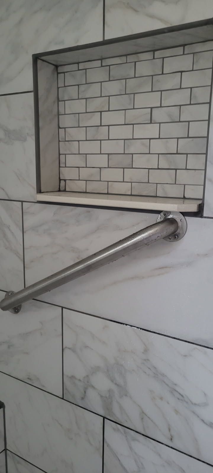 Silver grab bar in a tiled shower with a recessed shelf.