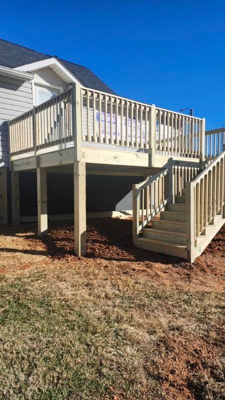 Wooden deck with stairs attached to a house; set on a brown mulch and dead grass; blue sky.