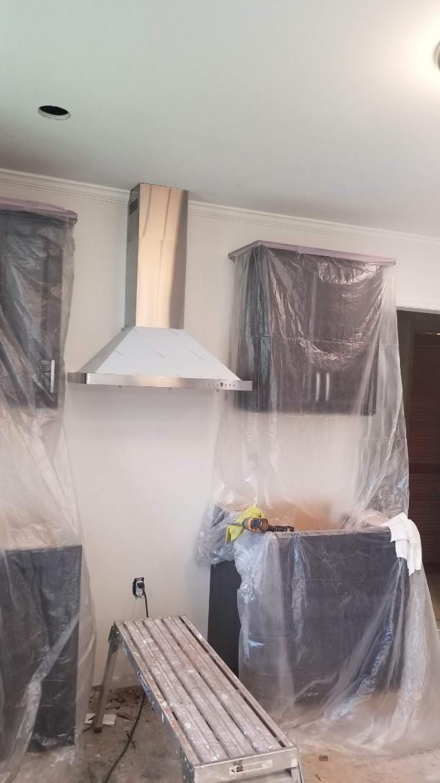 Kitchen with a stainless steel range hood, cabinets covered in plastic, and a stepladder.