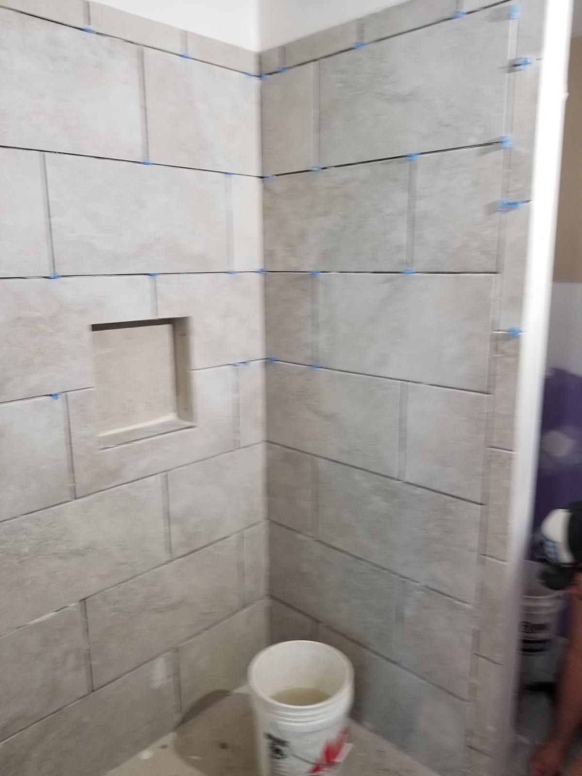 Tiled shower stall in progress with a niche, using gray rectangular tiles.