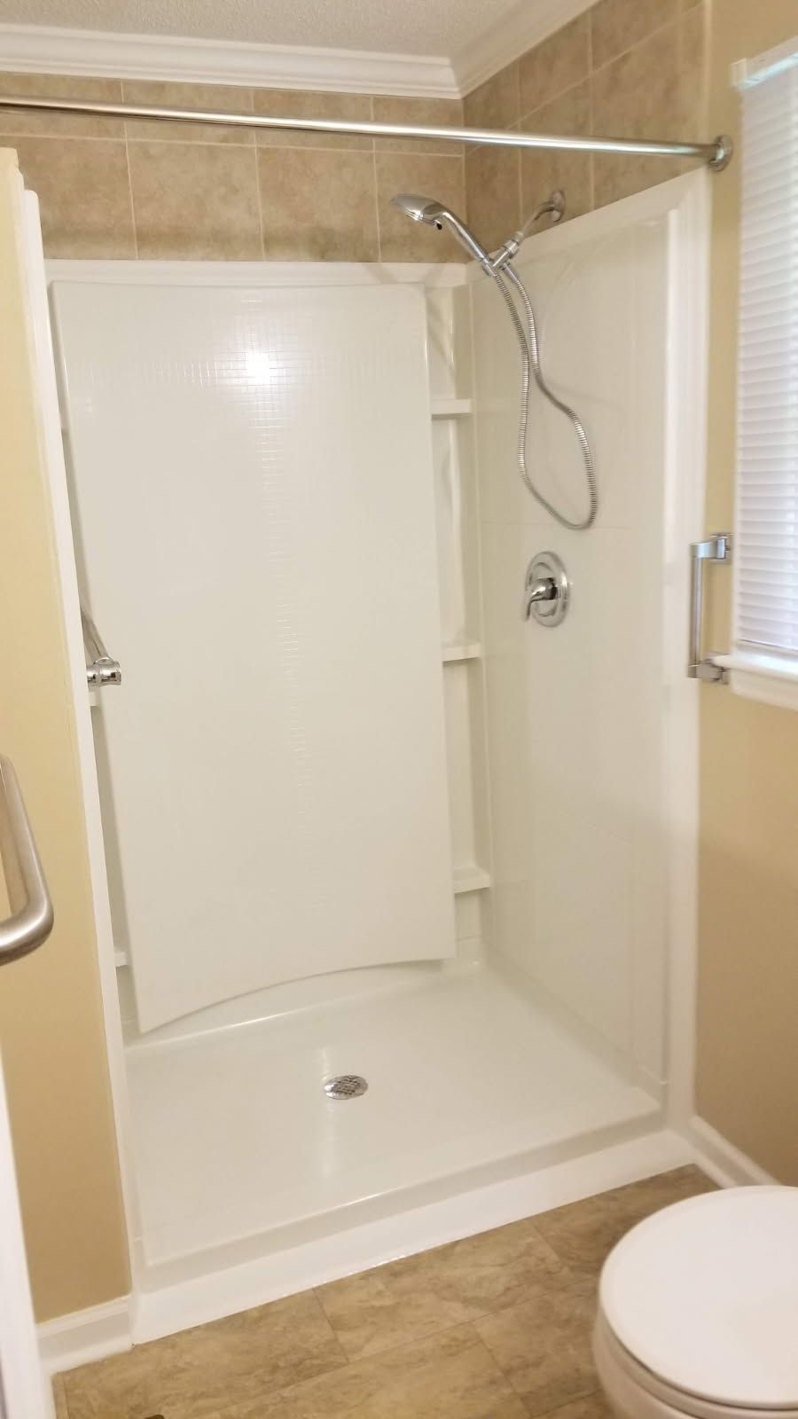 White shower stall with a grab bar, showerhead, and a closed door.