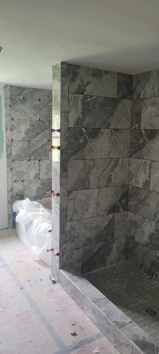Bathroom with tiled walls and floor, under construction. Gray tiles and a shower curb are visible.