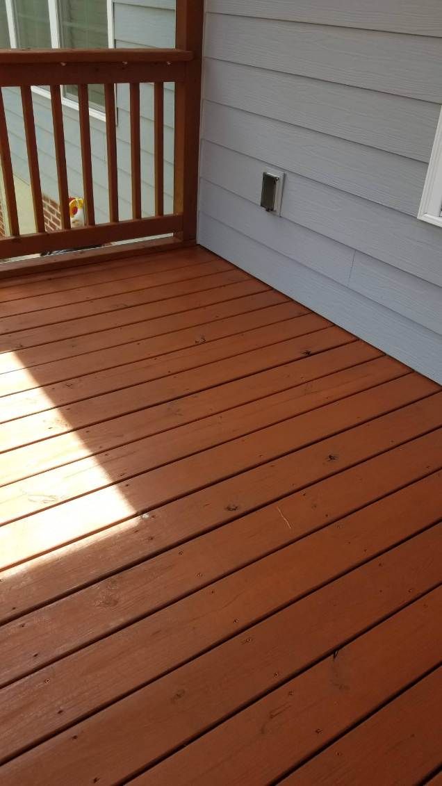 Brown wooden deck with railings, next to gray siding.