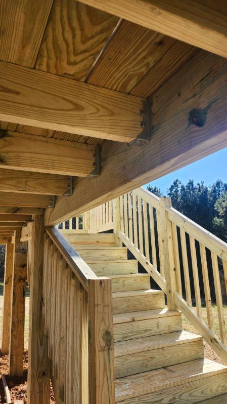 Wooden staircase leading up to a deck, viewed from below. Light brown wood, blue sky visible.
