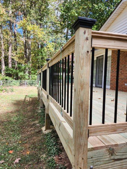 Wooden deck with black railing and black post caps, next to a grassy area and trees.