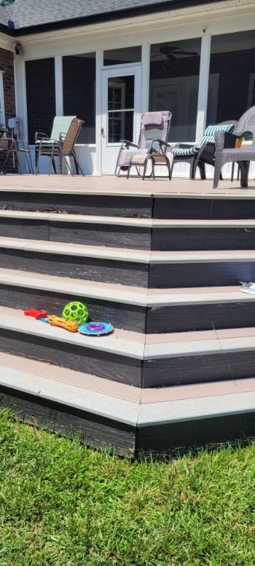 A multi-level gray deck with toys and chairs on the deck. Green grass in the foreground.