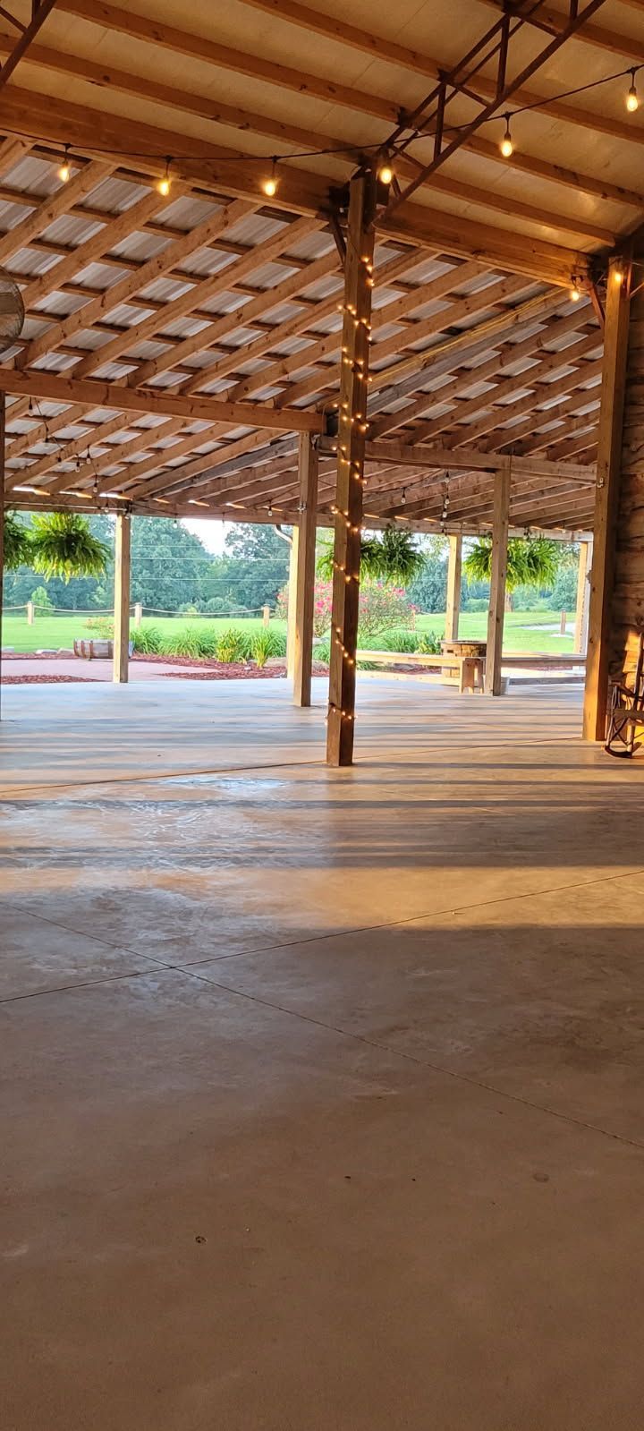 Inside view of a large barn with string lights, concrete floor, and hanging plants.