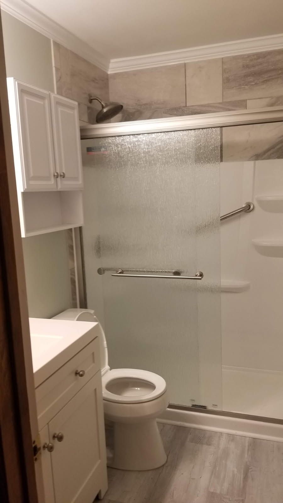 Bathroom with shower stall, toilet, vanity, and cabinet; neutral colors.