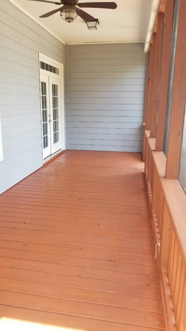Covered porch with orange wooden floor and railing, light blue wall, and white double doors.