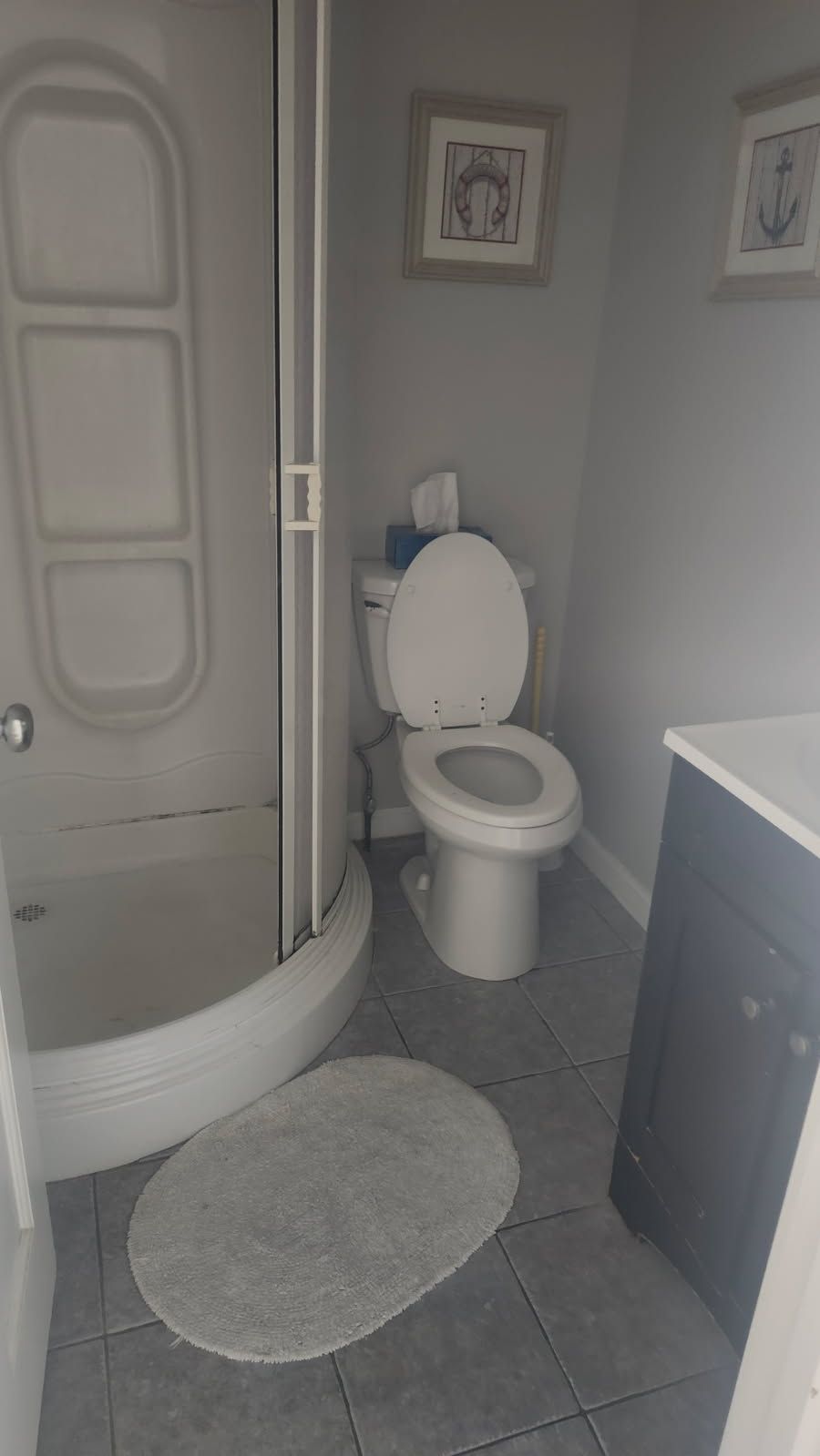 Small bathroom with a toilet, shower, and vanity. Gray walls and floor, neutral tones.