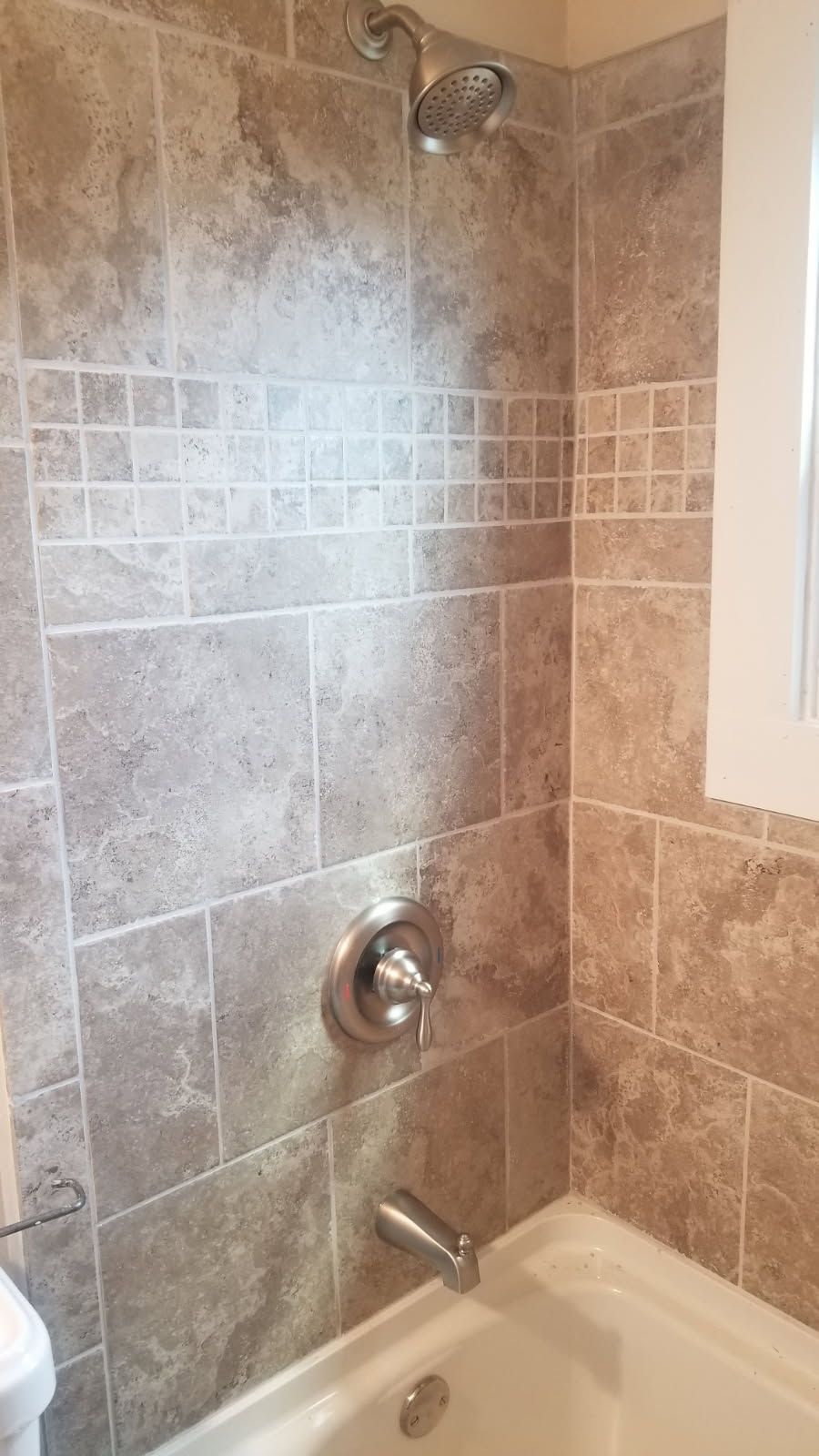 Tiled shower in a bathroom with a showerhead, faucet, and a bathtub. Beige tiles with a mosaic accent.