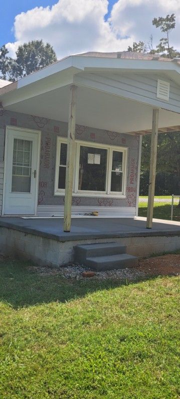 A small, single-story house with a porch and steps, surrounded by green grass. Overcast sky.