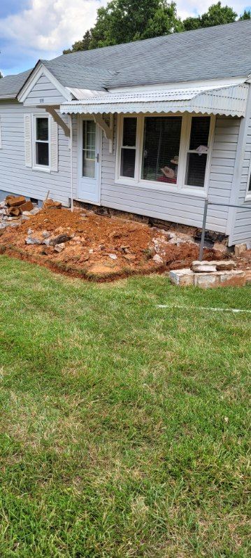 Excavation in front of a white house with a green lawn.