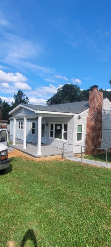 A light blue house with white pillars and a brick chimney on a green lawn under a bright blue sky.