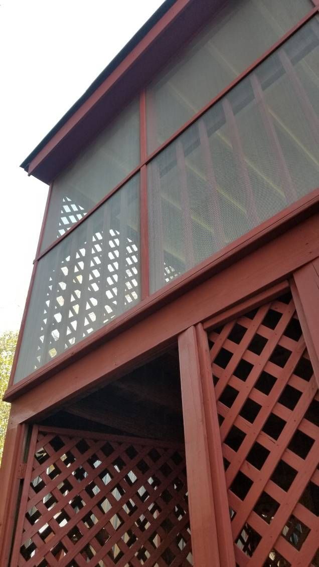Red wooden screened-in porch with lattice details. Exterior shot, angled upwards.