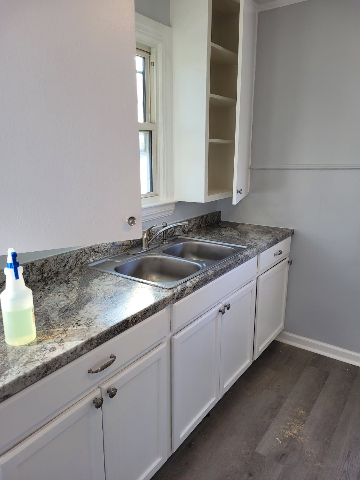 White kitchen cabinets, gray countertop, double sink, and a window.