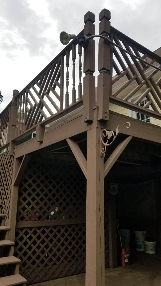 Brown wooden deck with railings, lattice, and support beams. A spotlight is mounted.