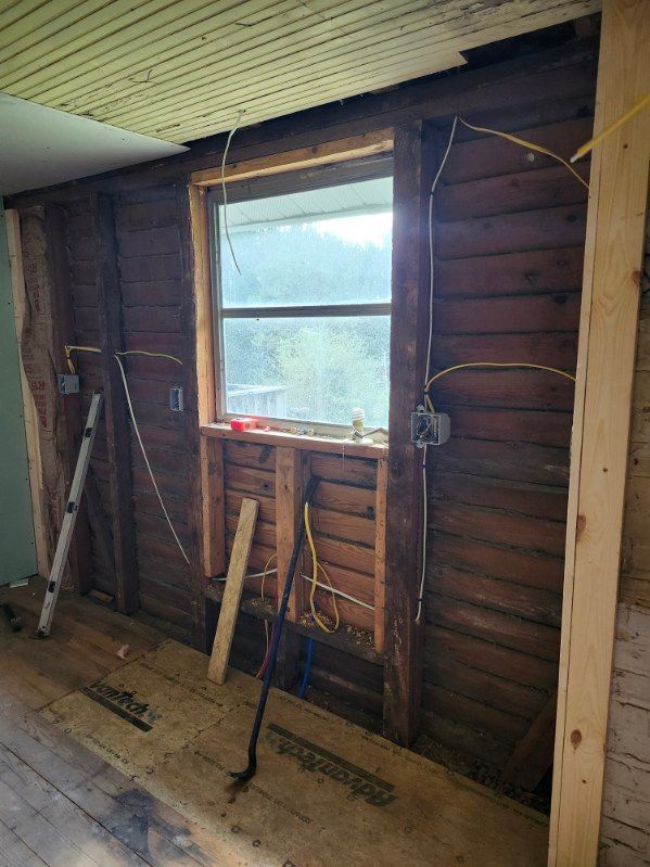 Interior room undergoing renovation, exposed wood wall with window, electrical wiring visible.