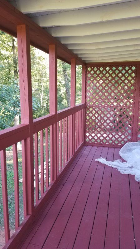 Red painted porch with lattice, railing, and roof. Trees visible outside.