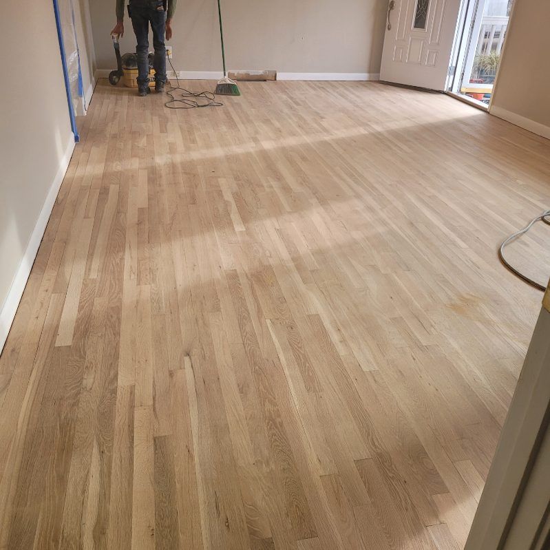 Newly sanded hardwood floor with a person standing near sanding equipment.