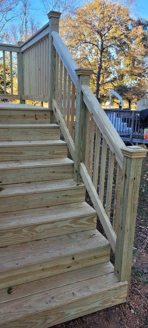 Wooden outdoor staircase with railing, leading up to a deck. Autumn foliage in background.