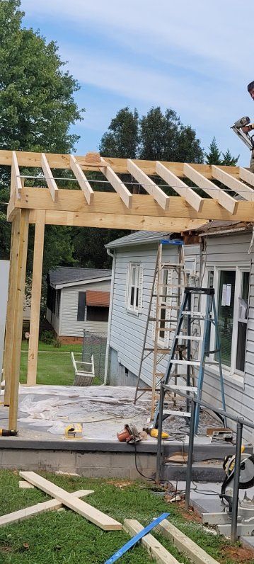 Construction of a wooden pergola attached to a light blue house, with a ladder and tools present.