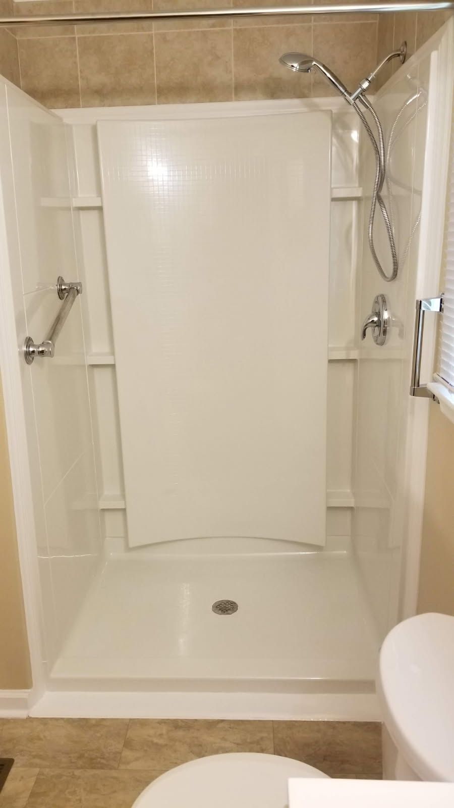 White accessible shower stall with grab bars, showerhead, and a center panel.