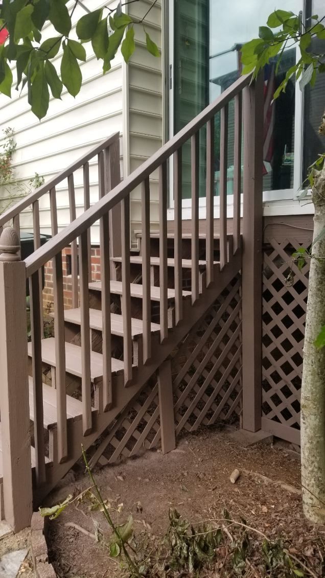 Wooden outdoor staircase with latticework siding, leading up to a house. Brown railing, steps, and structure.