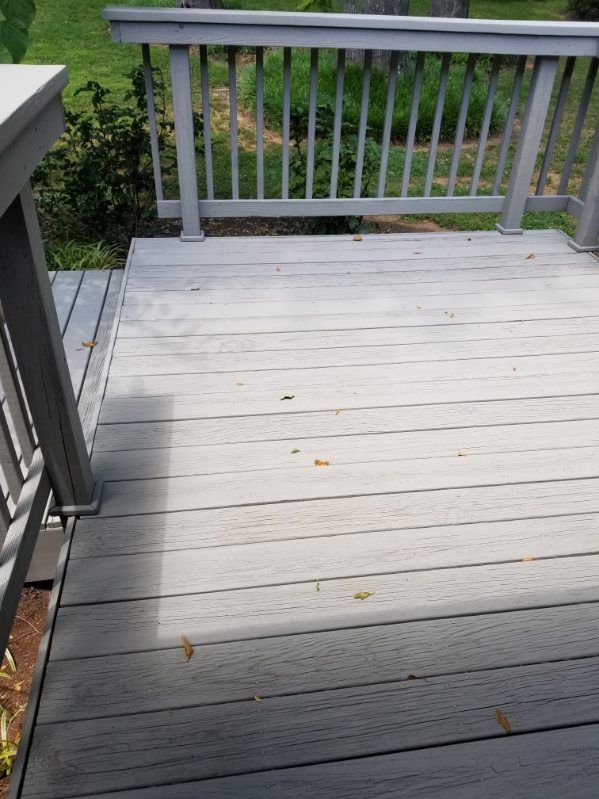 Gray wooden deck with railing, leaves scattered on the surface.
