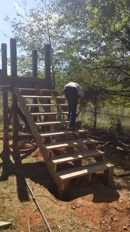 Person building wooden outdoor stairs to a platform. Sunny day, surrounded by trees.