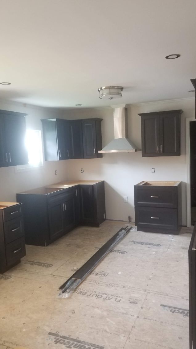 Kitchen under renovation with dark cabinets, a stainless steel range hood, and light-colored countertops.