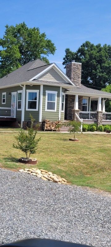 Green house with stone chimney and porch under a blue sky.  Lawn and gravel driveway.