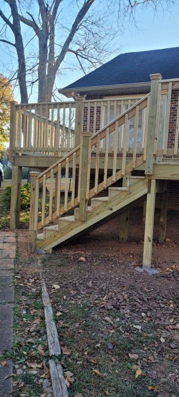 A wooden deck with stairs attached to a house. The steps lead down to a leaf-covered yard.