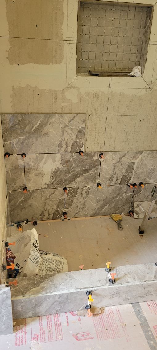 Wall with installed tiles, leveling clips. Mortar and exposed brick niche. Construction in progress.