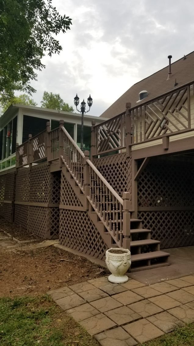 Brown wooden deck with lattice and stairs leading up to a screened porch, cloudy sky.
