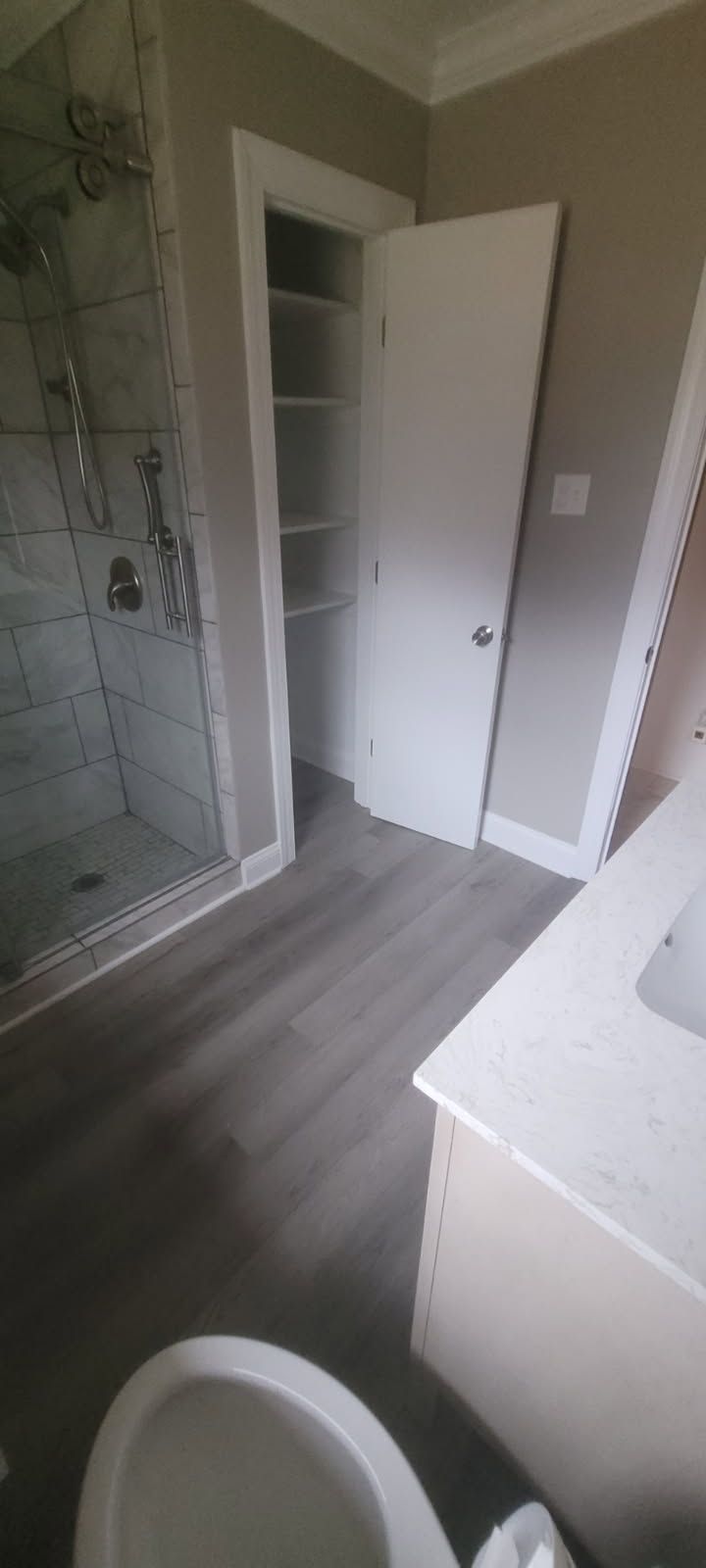 Bathroom with a shower, a cabinet, a toilet, and a closet with shelves. The floor is grey, and the walls are light-colored.