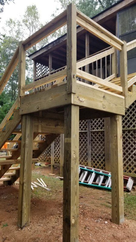 Wooden deck under construction with staircase and railing. Green and brown tones, outdoor setting.