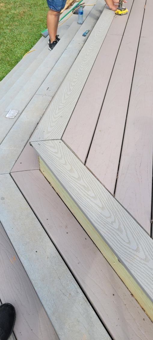 Person constructing deck steps outdoors; composite materials, tools visible.