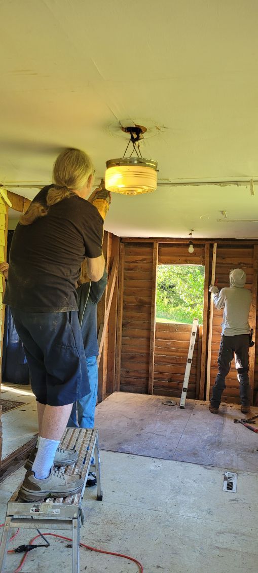 People working on a room renovation, one on a step stool near the ceiling, others near a doorway.