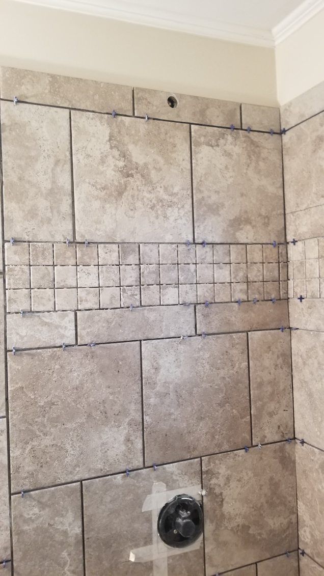 Tiled shower wall with a mosaic accent. Beige and gray tiles with a black faucet.